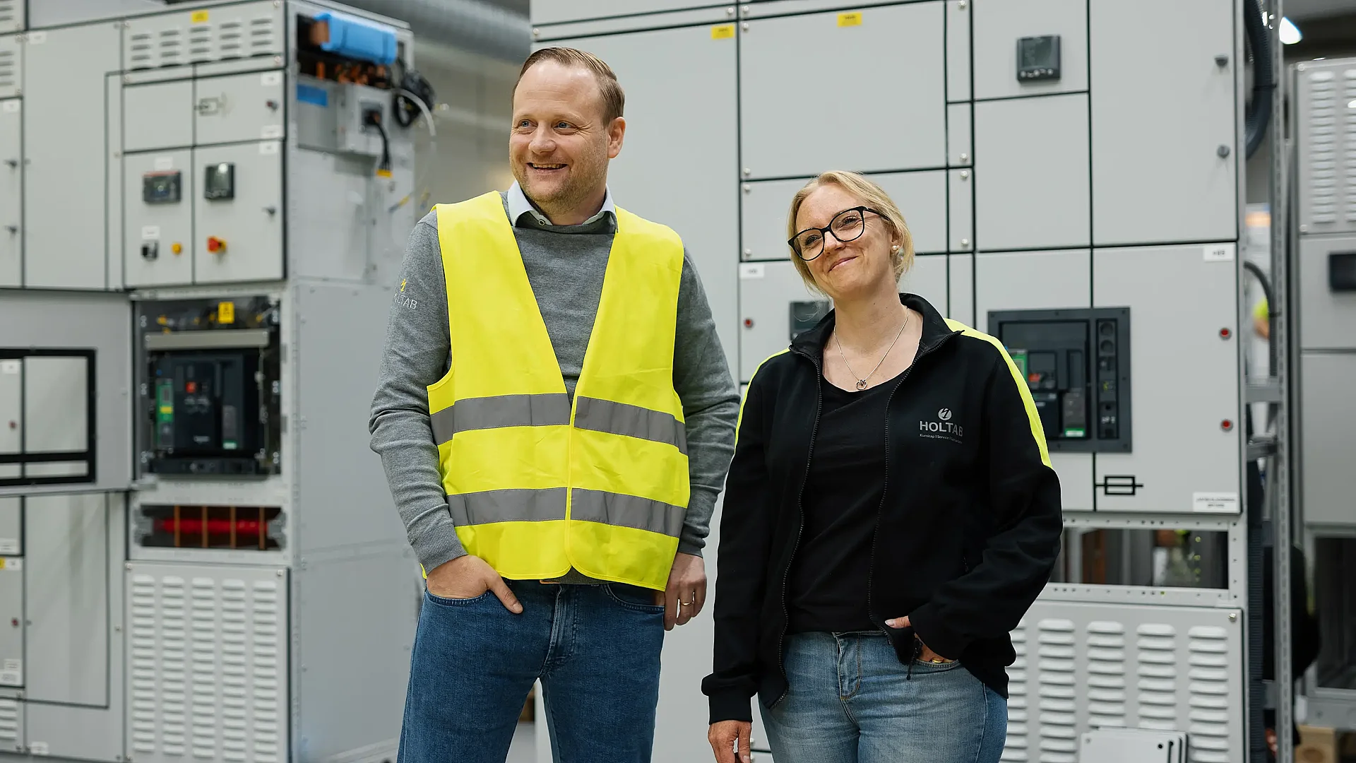 Kvinna och man står tillsammans framför ett ställverk i Holtabs produktion
